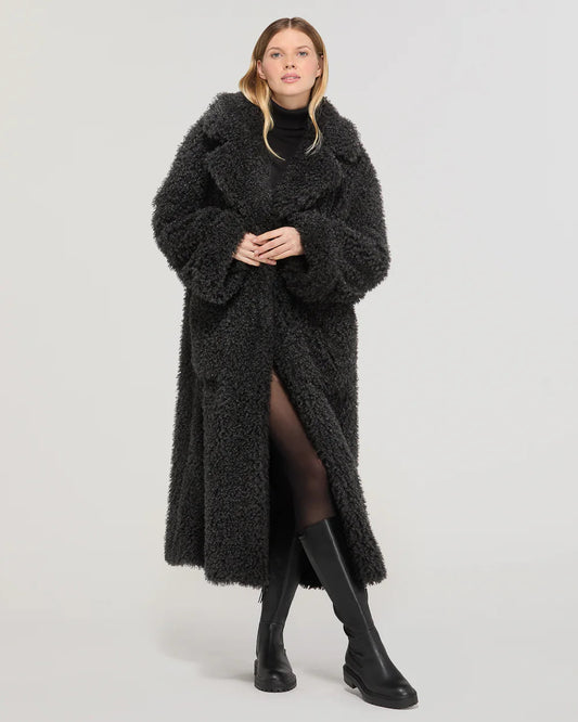 Donna con cappotto lungo oversize nero eco pelliccia, stivali alti neri, fondo neutro