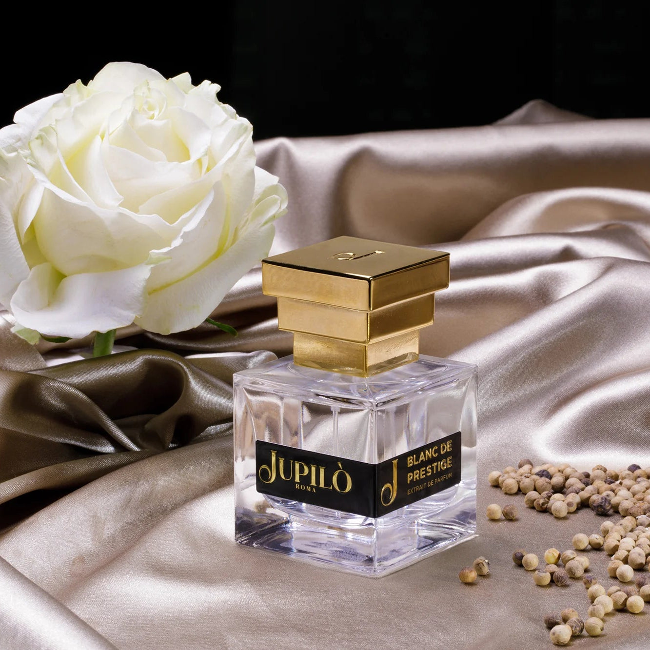 Flacone di profumo di lusso con tappo dorato su seta champagne, rosa bianca e grani aromatici