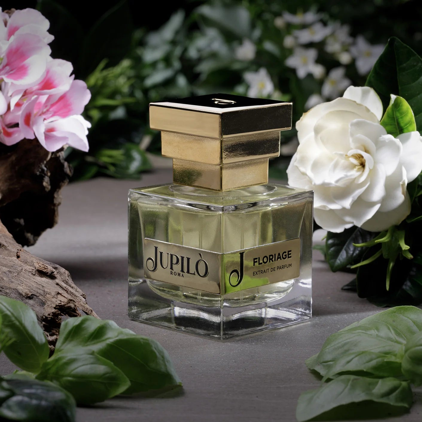 Flacone di profumo Floriage Jupilo con tappo dorato tra fiori freschi e foglie verdi
