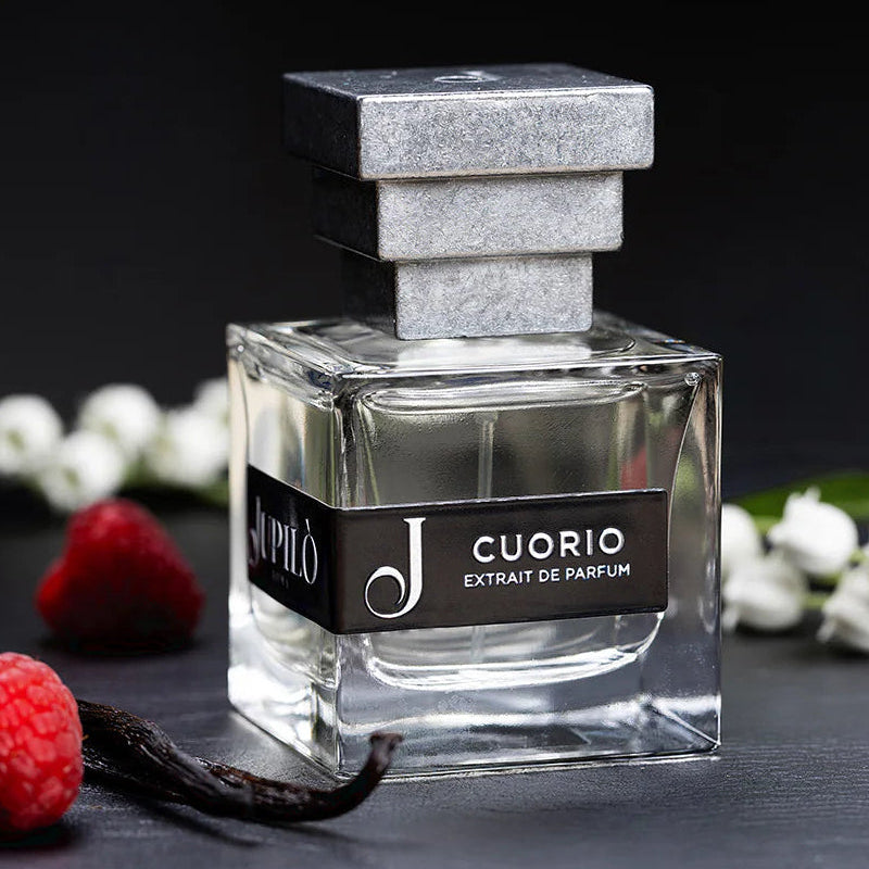 Bottiglia di profumo Cuorio Extrait de Parfum con tappo argentato, accanto a lamponi e vaniglia