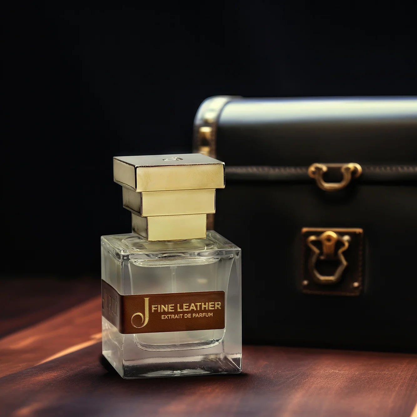 Bottiglia di profumo Fine Leather con tappo dorato accanto a borsetta elegante nera su sfondo scuro