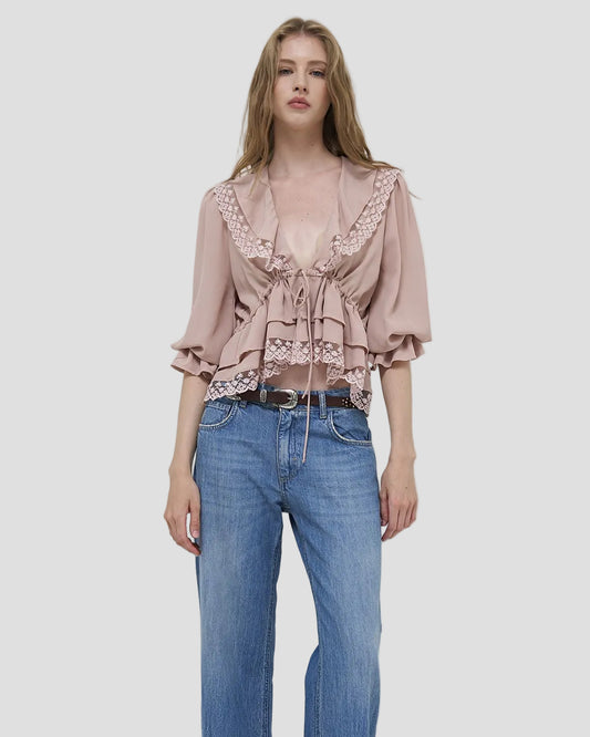 Modella con blusa fluida cipria con volant e pizzo, maniche a tre quarti, jeans casual.