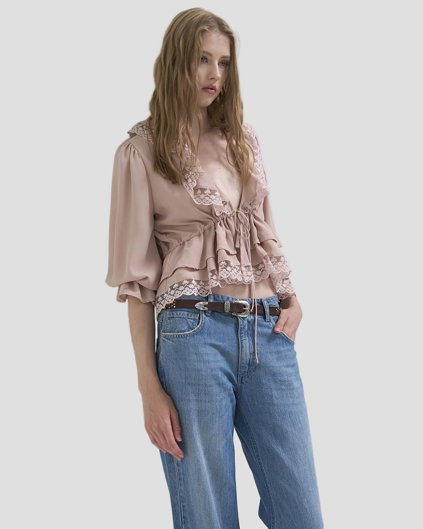 Blusa fluida cipria con pizzo indossata da donna, abbinata a jeans a vita alta.