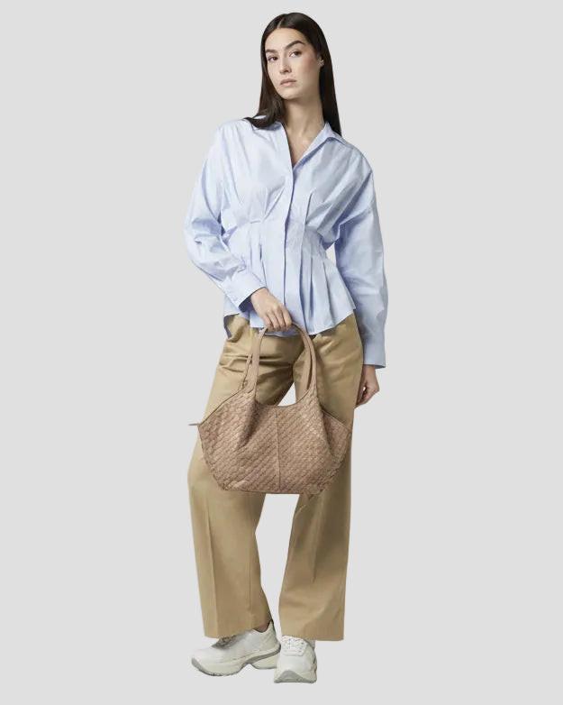 Modella con borsa intrecciata in pelle beige, camicia azzurra e pantaloni beige, stile elegante