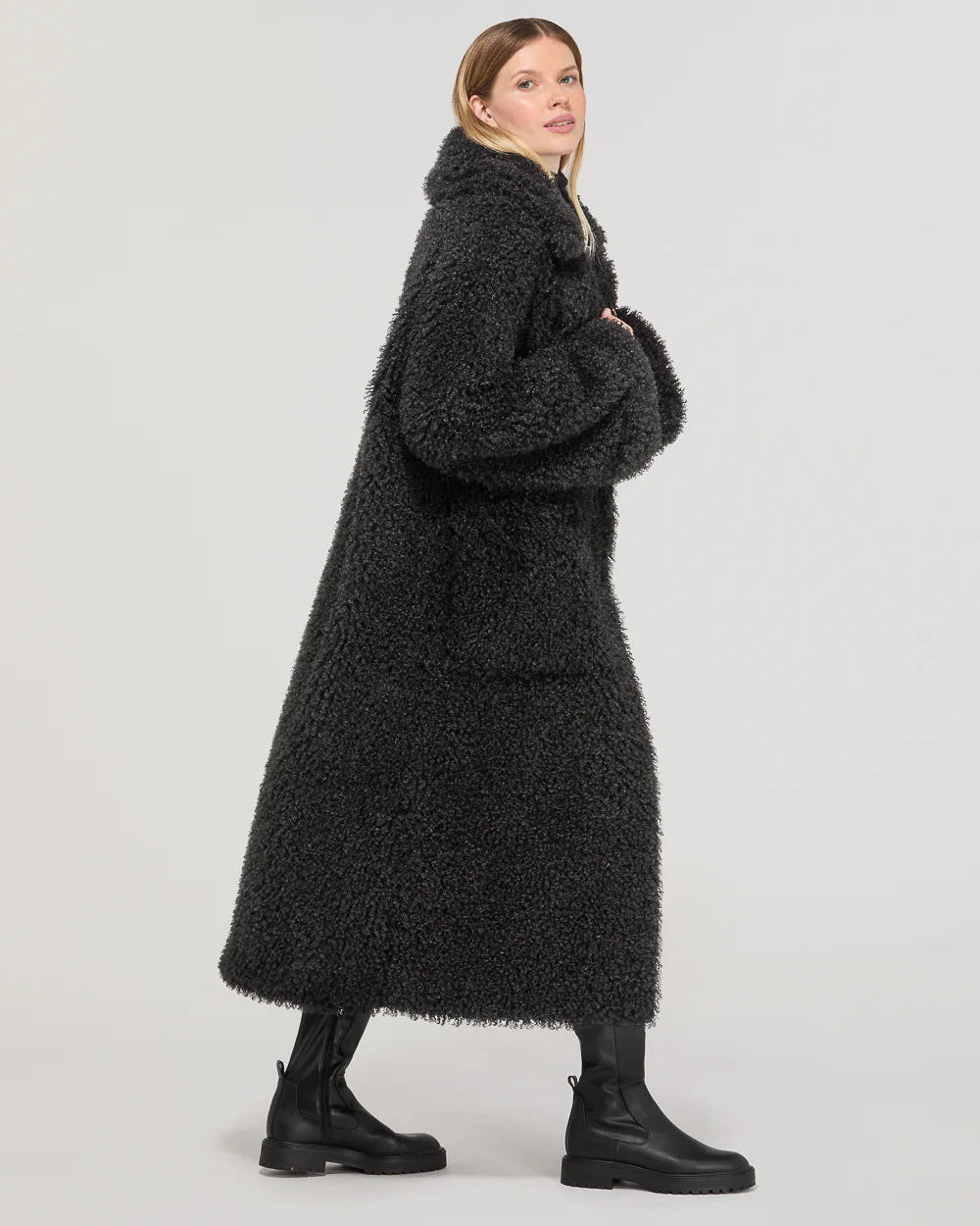 Donna indossa cappotto lungo oversize nero eco, stivali alti neri, fondo chiaro