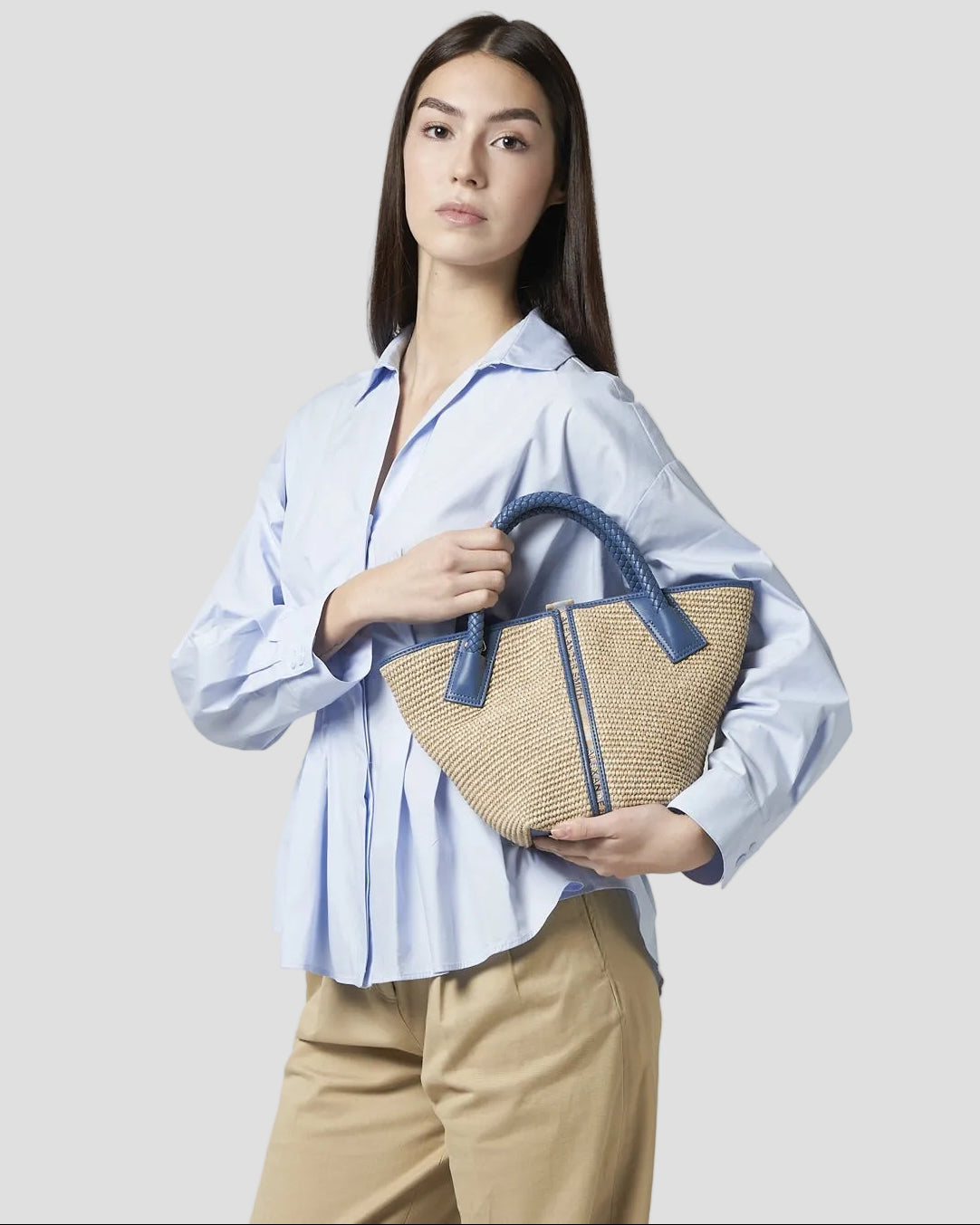 Donna con borsa a mano in rafia beige e manico intrecciato in pelle azzurro, look elegante.