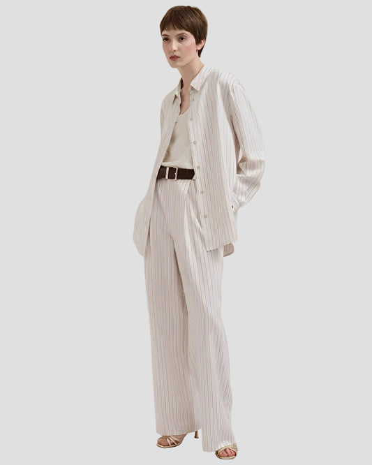 Donna con pantaloni gessati color burro, camicia coordinata e sandali eleganti
