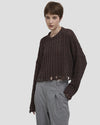 Modella con pullover marrone a trecce, taglio corto e bordi sfrangiati, stile casual elegante.
