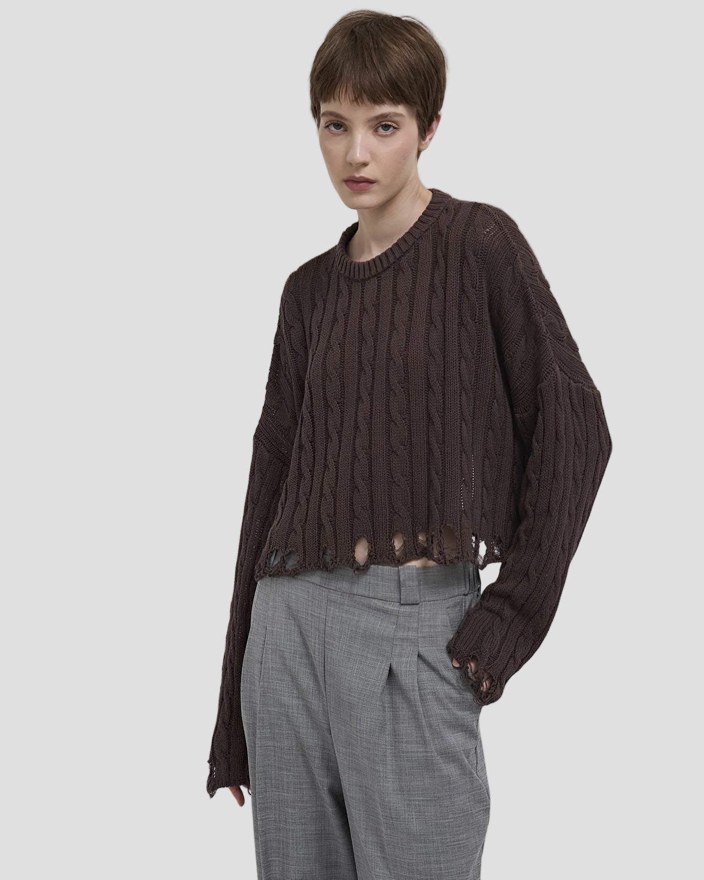 Modella con pullover marrone a trecce, taglio corto e bordi sfrangiati, stile casual elegante.