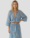 Modella a figura intera indossa il top Pho Firenze composto da top cropped azzurro scollato con nappe lunghe e gonna midi coordinata con stampa a rilievo