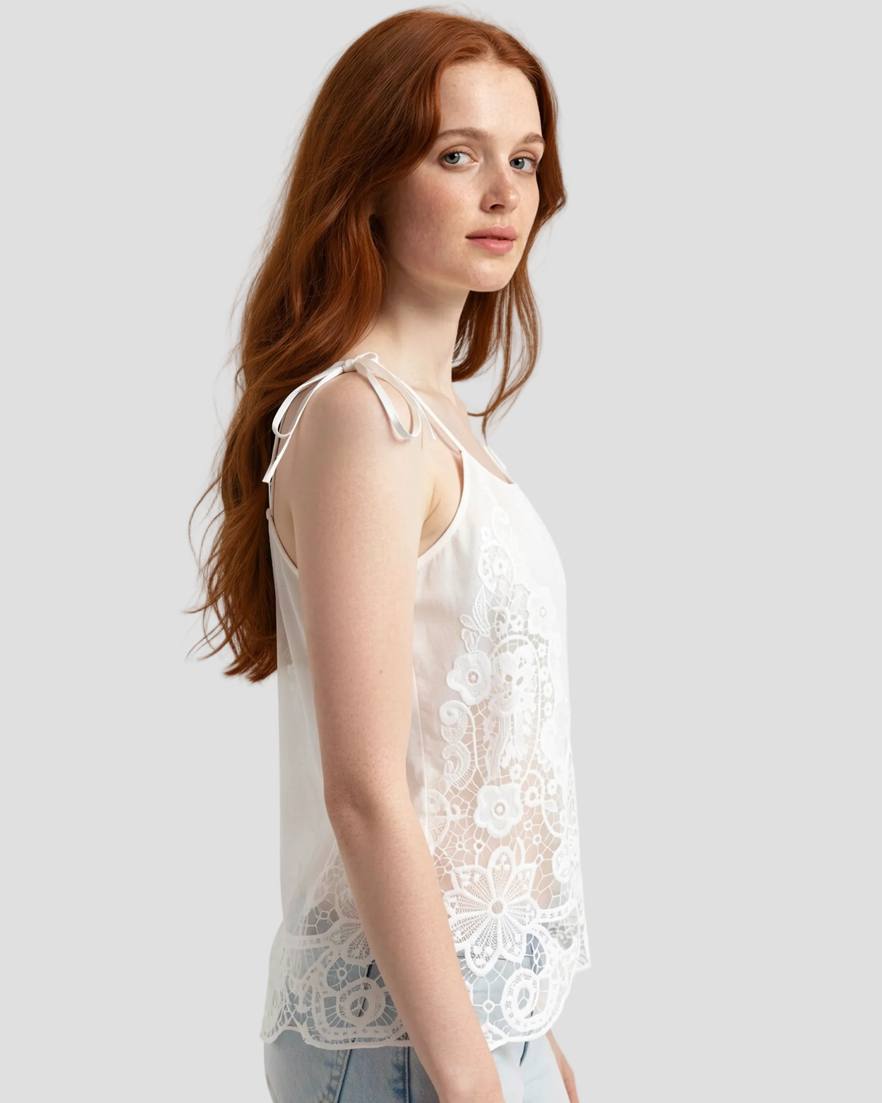Top bianco donna in cotone con ricami pizzo frontali, canotta interna e
spalline a fiocco, modella di lato 
