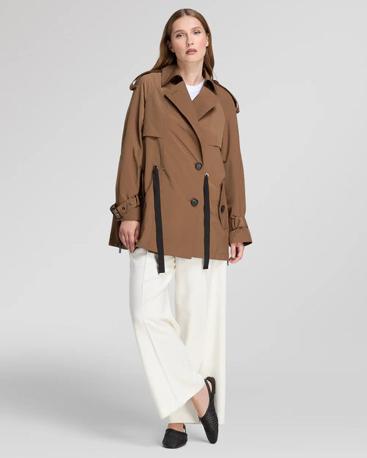 Donna indossa trench corto marrone elegante con cintura e pantaloni bianchi ampi, sfondo neutro. diego M